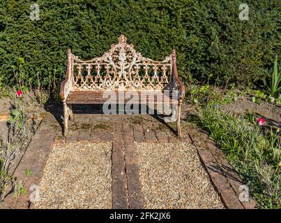 Eine schäbige, schicke, dekorative, rostig weiß lackierte Metallbank im Garten im Dunsborough Park, Ripley, Surrey, Südostengland Stockfoto