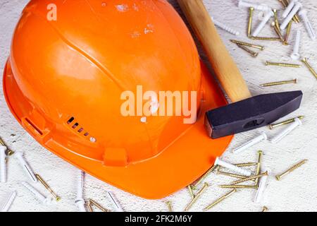 Orangefarbener Schutzhelm mit Klauenhammer auf hellgrauem Zement. Hausreparatur und Verbesserung, Hausbau Konzept. Stockfoto