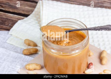 Frische hausgemachte knusprige Erdnussbutter mit Nüssen auf hellem Holzhintergrund in der Küche. Stockfoto
