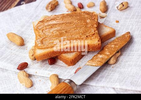 Hausgemachtes Toast zum Frühstück mit frischer knackiger Erdnussbutter und Nüssen auf hellem Textilhintergrund. Stockfoto