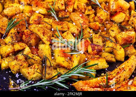 Frisch gebackene Kürbisstücke mit Rosmarin und Gewürzen auf schwarzem Metallpfannenhintergrund. Stockfoto