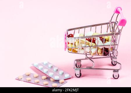 Warenkorb mit verschiedenen medizinischen Pillen und Kapseln darin auf rosa Hintergrund. Pharmakologie und Drogeriekonzept. Stockfoto