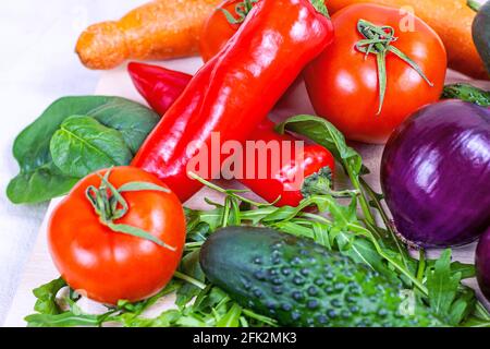 Frisches Bauerngemüse für den Salat: Gurken, Tomaten, Zwiebeln, Paprika, Rucola-Blätter in der Küche auf hellem Hintergrund. Stockfoto