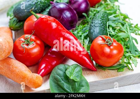 Frisches Bauerngemüse für den Salat: Gurken, Tomaten, Zwiebeln, Paprika, Rucola-Blätter in der Küche auf hellem Hintergrund. Stockfoto