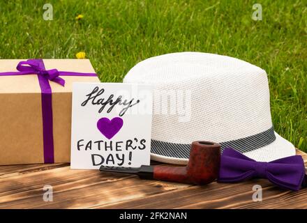 Grußkarte Happy Father's Day mit Geschenkbox und Herren Accessoires auf einem rustikalen Holztisch und Grashintergrund Stockfoto