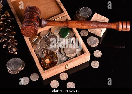 Eine hölzerne Schatzkiste voller Silbermünzen und Edelsteine, umgeben von losen verschütteten Münzen mit Gavel. Stockfoto