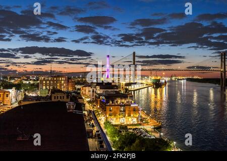Skyline von Savannah Georgia bei Sonnenuntergang von der Spitze einer Dachterrasse mit Flusswasser, Brücke und Gebäuden Stockfoto