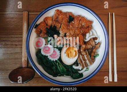 Asiatische Suppe mit udon-Nudeln, Huhn, gekochten Eiern und Spinat in einer Schüssel auf dem Tisch. Horizontale Ansicht von oben Stockfoto