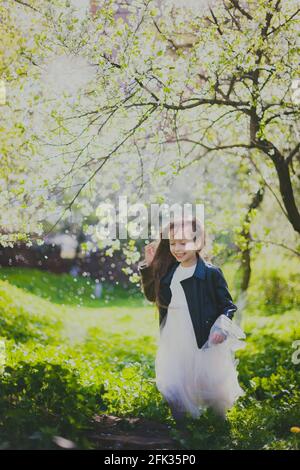 Kleines Mädchen in schwarzer Jacke und weißem Kleid tanzen in Der Kirschgarten im Frühling Stockfoto