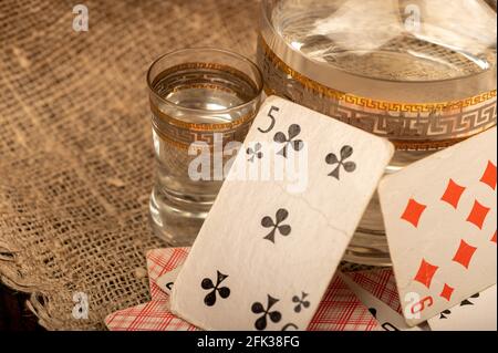 Spielkarten, ein Glas Wodka und ein Dekanter Wodka auf einem Tisch, der mit grobem Sackleinen bedeckt ist. Nahaufnahme, selektiver Fokus. Stockfoto