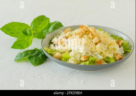 Traditioneller caesar-Salat auf einem Teller auf einem weißen Tisch mit Blättern, Sauce, Croutons und Parmesan Stockfoto