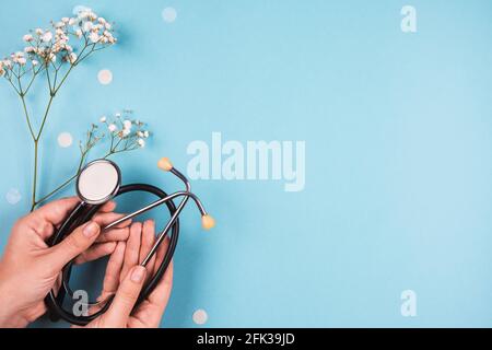 Phonendoskop in weiblichen Händen auf blauem Hintergrund mit Blumen. Stockfoto