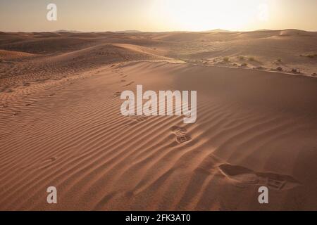 Sonnenuntergang über den Sanddünen mit Fußabdrücken in der Wüste. Die Geisterstadt Al-Madam liegt etwa 60 km von Dubai City entfernt. vereinigte arabische emirate. Das Konzept Stockfoto