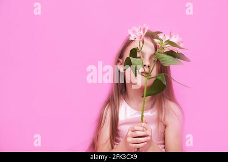 Alstroemeria in der Hand der Mädchen auf einem rosa Hintergrund. Kleines Mädchen schließt die Augen. Hochwertige Fotos Stockfoto