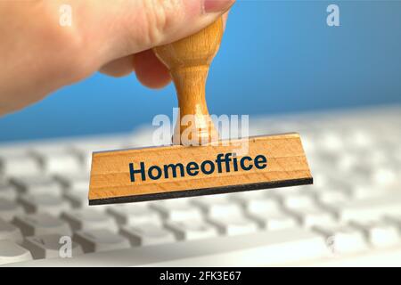 Deutschland. April 2021. Ein Holzstempel mit der Aufschrift „Homeoffice“, der von einer Hand in einem Bluten über einer weißen Computertastatur gehalten wird. Foto mit Komposition vor blauem Hintergrund. Das Home Office ist an der Tagesordnung und wird, wo immer möglich, von Experten empfohlen. Credit: dpa/Alamy Live News Stockfoto