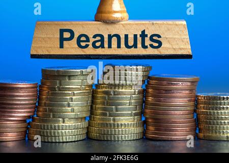 Deutschland. April 2021. Eine Holzmarke mit der Aufschrift 'Peanuts' über mehrere Stapel Euro/Cent-Münzen. Foto mit Komposition vor blauem Hintergrund. Erdnüsse sind umgangssprachlich ein Ausdruck für kleine Dinge oder unbedeutende Geldsummen. Das Wort wurde zum deutschen Wort des Jahres 1994 erklärt.Quelle: dpa/Alamy Live News Stockfoto