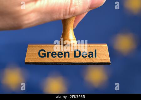 Deutschland. April 2021. Ein symbolischer Holzstempel mit der Aufschrift „Green Deal“, der von einer Hand in einem Bluten vor einer verschwommenen EU-Flagge im Hintergrund gehalten wird. Foto mit Komposition [M]. Der European Green Deal ist ein von der Europäischen Kommission vorgebautes Konzept mit dem Ziel, die Netto-Treibhausgasemissionen in der Europäischen Union bis 2050 auf Null zu reduzieren und der erste klimaneutrale Kontinent zu werden. Das Green Deal soll zu einem zentralen Bestandteil der Klimapolitik der Europäischen Union werden. Credit: dpa/Alamy Live News Stockfoto