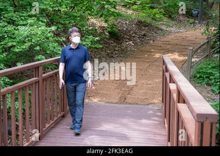 Asiatischer Mann mittleren Alters, der allein in einem Waldweg mit Gesichtsmaske geht. Stockfoto