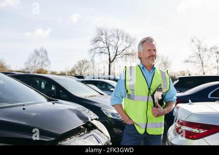 Reifer männlicher Verlustrenner trägt eine Warnweste, die im Stehen steht Compound for Damaged Cars Compiling Insurance Claim Report on digital Tablet Stockfoto