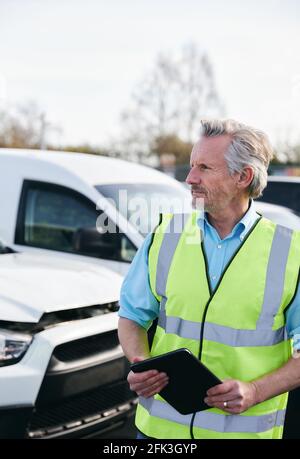 Reifer männlicher Verlustrenner trägt eine Warnweste, die im Stehen steht Compound for Damaged Cars Compiling Insurance Claim Report on digital Tablet Stockfoto