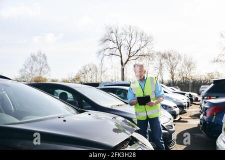 Reifer männlicher Verlustrenner trägt eine Warnweste, die im Stehen steht Compound for Damaged Cars Compiling Insurance Claim Report on digital Tablet Stockfoto