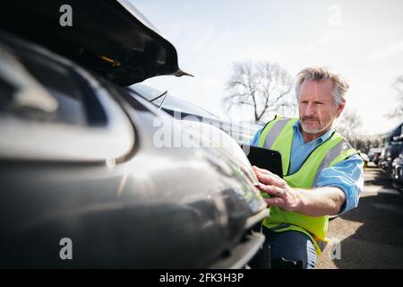 Reifer männlicher Verlustrenner trägt eine Warnweste, die im Stehen steht Compound for Damaged Cars Compiling Insurance Claim Report on digital Tablet Stockfoto