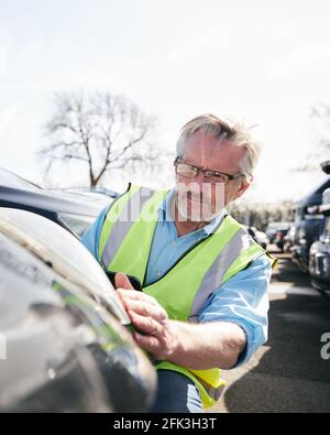 Reifer männlicher Verlustrenner trägt eine Warnweste, die im Stehen steht Compound for Damaged Cars Compiling Insurance Claim Report on digital Tablet Stockfoto