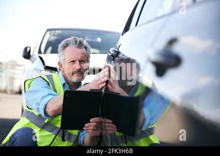 Reifer männlicher Verlustrenner trägt eine Warnweste, die im Stehen steht Compound for Damaged Cars Compiling Insurance Claim Report on digital Tablet Stockfoto