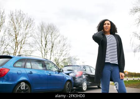 Junge Frau reibt Hals in Schmerzen von Schleudertrauma Verletzung stehen Durch beschädigtes Auto nach Verkehrsunfall Stockfoto