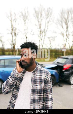 Junger Mann, der nach der Meldung von Verkehrsunfällen an einem beschädigten Auto steht Vorfall bei einer Versicherungsgesellschaft, die ein Mobiltelefon verwendet Stockfoto