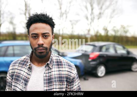 Porträt eines unversicherten männlichen Fahrers, der nach einem beschädigten Auto steht Verkehrsunfall, für den er verantwortlich ist Stockfoto