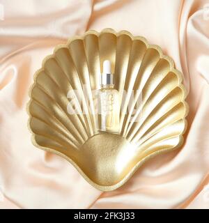 Goldene Perle Muschel Dekoration mit transparenter Tropfflasche mit Serum auf Pfirsichgewebe. Flach liegend, Draufsicht. Haarbehandlung Schönheit Produkt-Design. Stockfoto