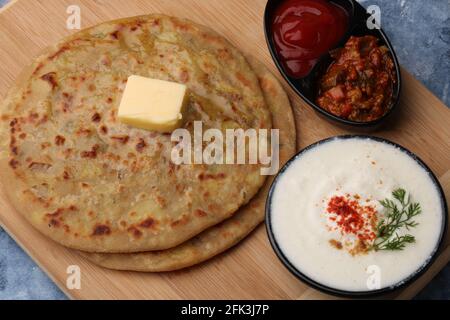 Traditionelles indisches Essen Aloo Paratha oder gefülltes Kartoffelbrot. Serviert mit eingelegtem Tomatenketchup und Quark, Butter, Zwiebelchili. Stockfoto