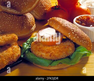 Hähnchenburger in entkerntem Brötchen mit Salat, Tomatenscheibe und Sauerrahm, Tomaten, Gebäck, Brötchen und Burgern auf hellem Holzboden Stockfoto