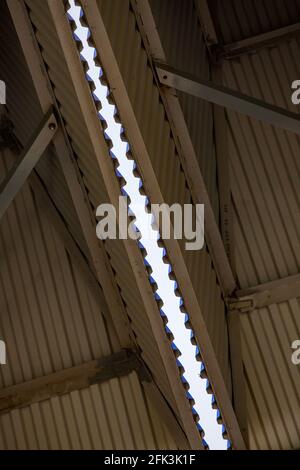 Geripptes Metallprofildach eines Industriegebäudes oder Hangars. Abstrakte Ansicht. Blauer Himmelsstreifen auf dem Hintergrund. Stockfoto
