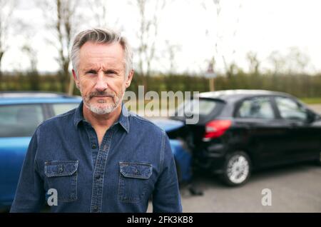 Porträt eines älteren männlichen Fahrers, der bei einem beschädigten Auto steht Seite der Straße nach einem Verkehrsunfall Stockfoto