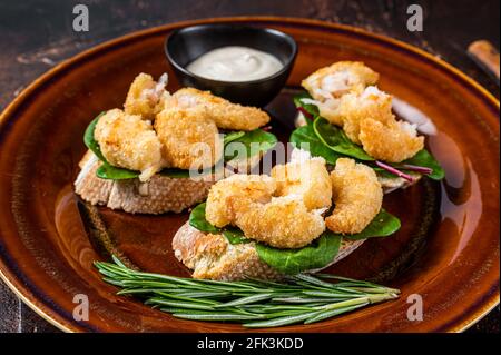 Sandwiches mit gebratenen Garnelen, Garnelen, Spinat und Mangold-Salat auf einem rustikalen Teller. Dunkler Hintergrund. Draufsicht Stockfoto
