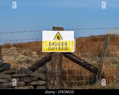 Gelbes Warnschild mit der Aufschrift „Danger Cliff Edge“ auf dem elektrischen Gerät Zaun Stockfoto