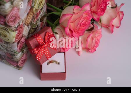 Goldener Ehering in einer roten Schachtel und ein Strauß rosa Rosen. Romantik. Heiratsantrag Stockfoto