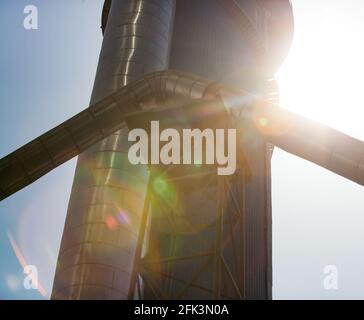 Silhouette des Zementwerks Turm (Silo) in Sonnenbeleuchtung mit farbigen Fackeln. Abstrakter industrieller Hintergrund. Stockfoto