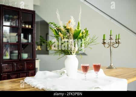 Eleganter Blumenstrauß auf einem Tisch, begleitet von zwei Cocktails Becher in einem geräumigen, modernen Haus Stockfoto