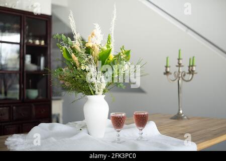 Eleganter Blumenstrauß auf einem Tisch, begleitet von zwei Cocktails Becher in einem geräumigen, modernen Haus Stockfoto