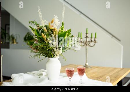 Eleganter Blumenstrauß auf einem Tisch, begleitet von zwei Cocktails Becher in einem geräumigen, modernen Haus Stockfoto