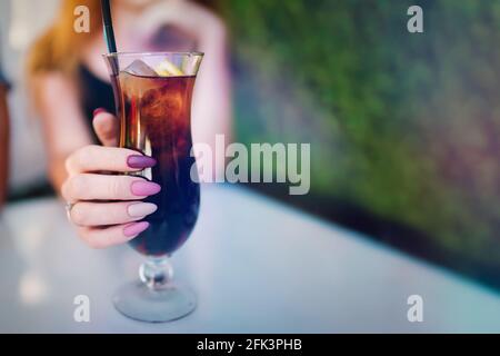 Mädchen Hand mit rosa und lila Maniküre halten Glas mit Cocktail. Frau in der Sommerbar genießt Eisgetränke. Lange lackierte Nägel. Nahaufnahme mit Kopierbereich. Stockfoto