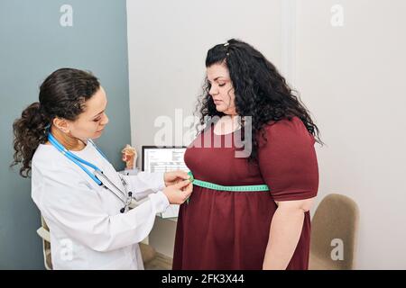Ernährungsberatung. Ernährungsberaterin untersucht die Taille einer Frau mit einem Maßband, um klinische Nahrung zu verschreiben Stockfoto