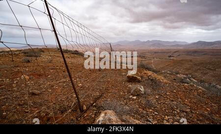 Einsame Wüstenlandschaft mit einem verlassenen Drahtzaun unter tief hängenden Wolken Stockfoto