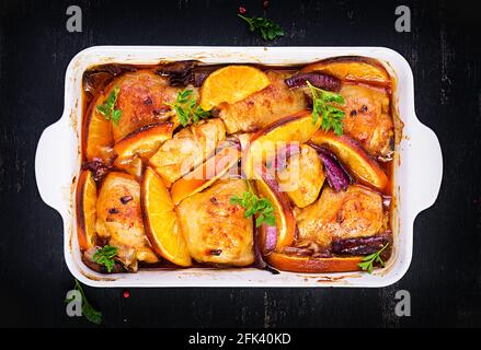 Gebackene Hähnchenschenkel. Appetitliche Scheiben gebackenes Huhn mit roten Zwiebeln und Orangen in einer Auflaufform. Draufsicht, Kopierbereich Stockfoto