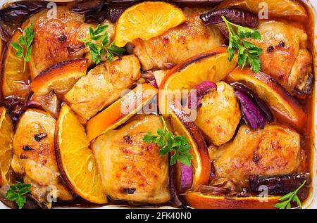 Gebackene Hähnchenschenkel. Appetitliche Scheiben gebackenes Huhn mit roten Zwiebeln und Orangen in einer Auflaufform. Draufsicht, Textur Stockfoto