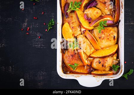 Gebackene Hähnchenschenkel. Appetitliche Scheiben gebackenes Huhn mit roten Zwiebeln und Orangen in einer Auflaufform. Draufsicht, Kopierbereich Stockfoto
