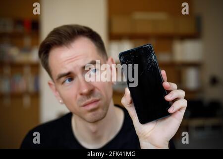 Der traurige Mann hält ein kaputtes Smartphone mit Rissen Stockfoto